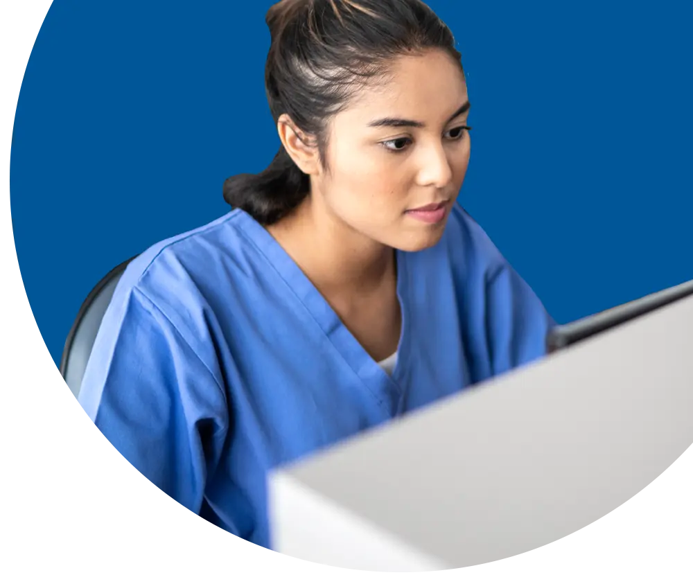 A woman wearing scrubs looks at a computer screen.