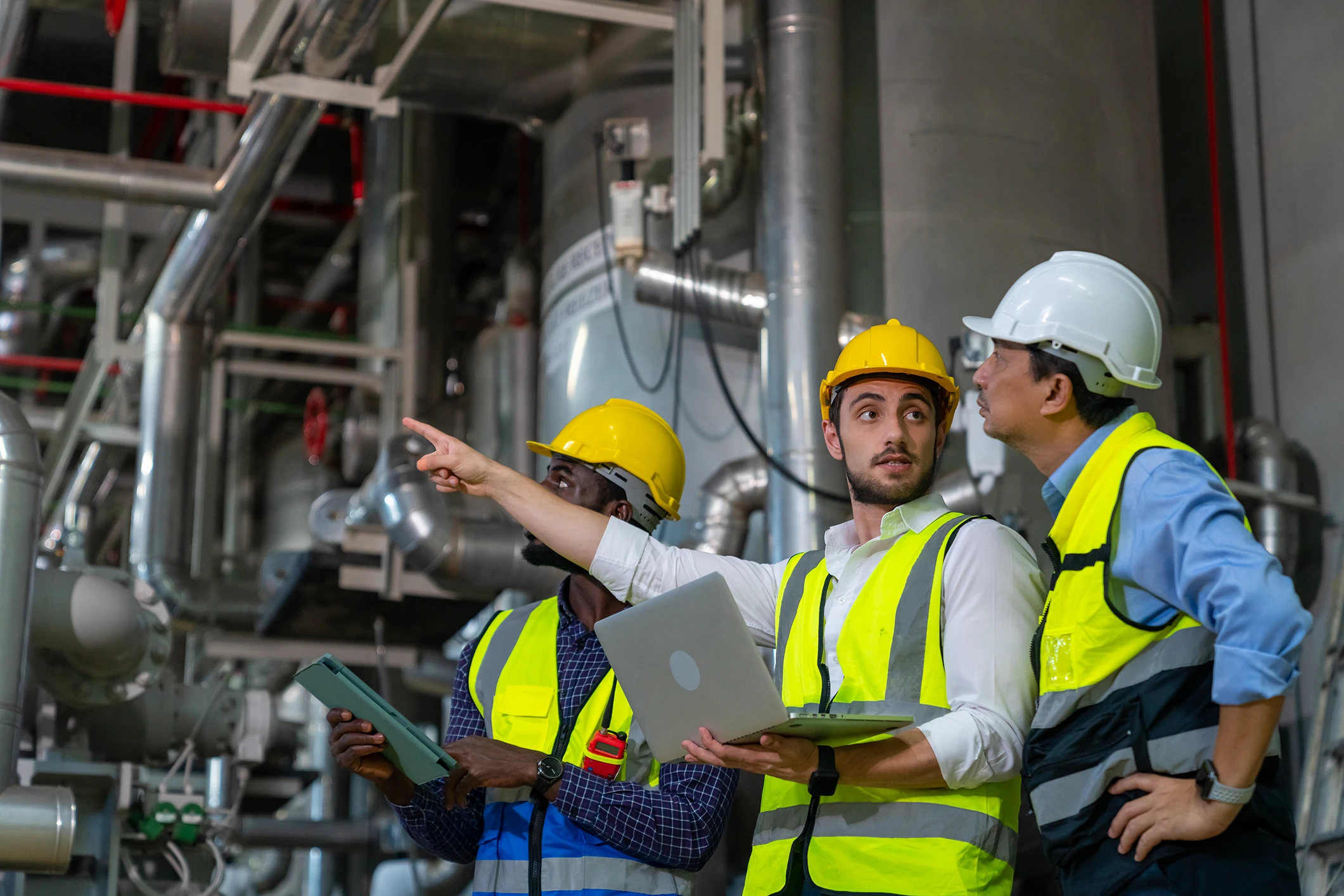 Two men wearing safety equipment look down on machining equipment