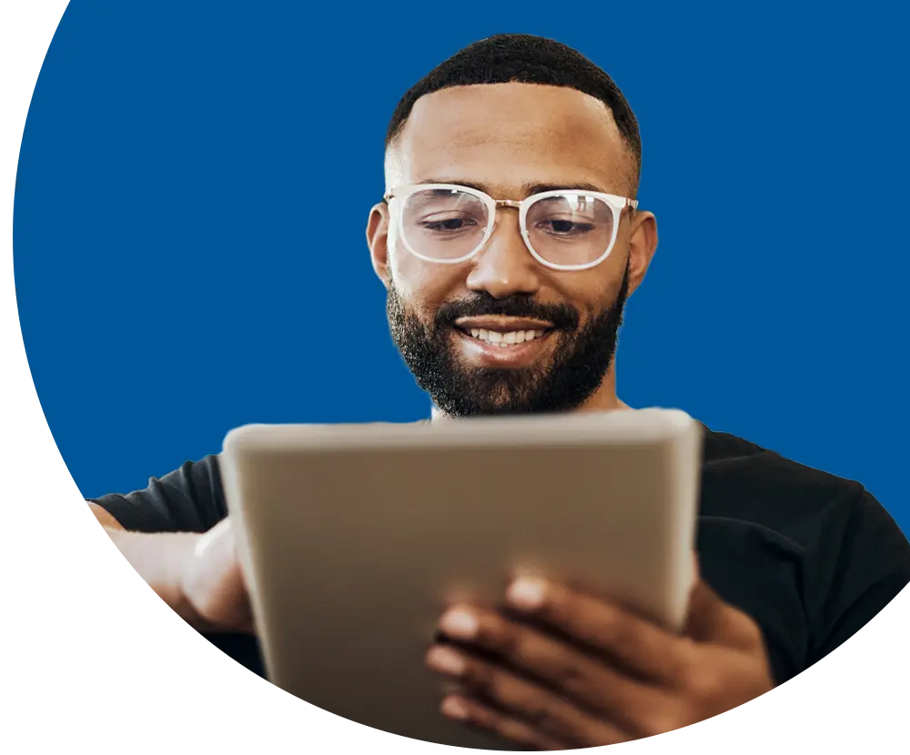 A man wearing glasses looks down at a tablet.